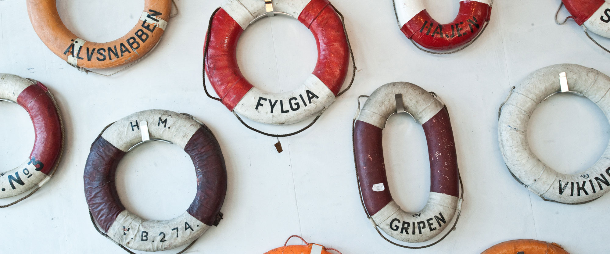 Livbojar med olika fartygsnamn skrivna på upphängda på en vägg.