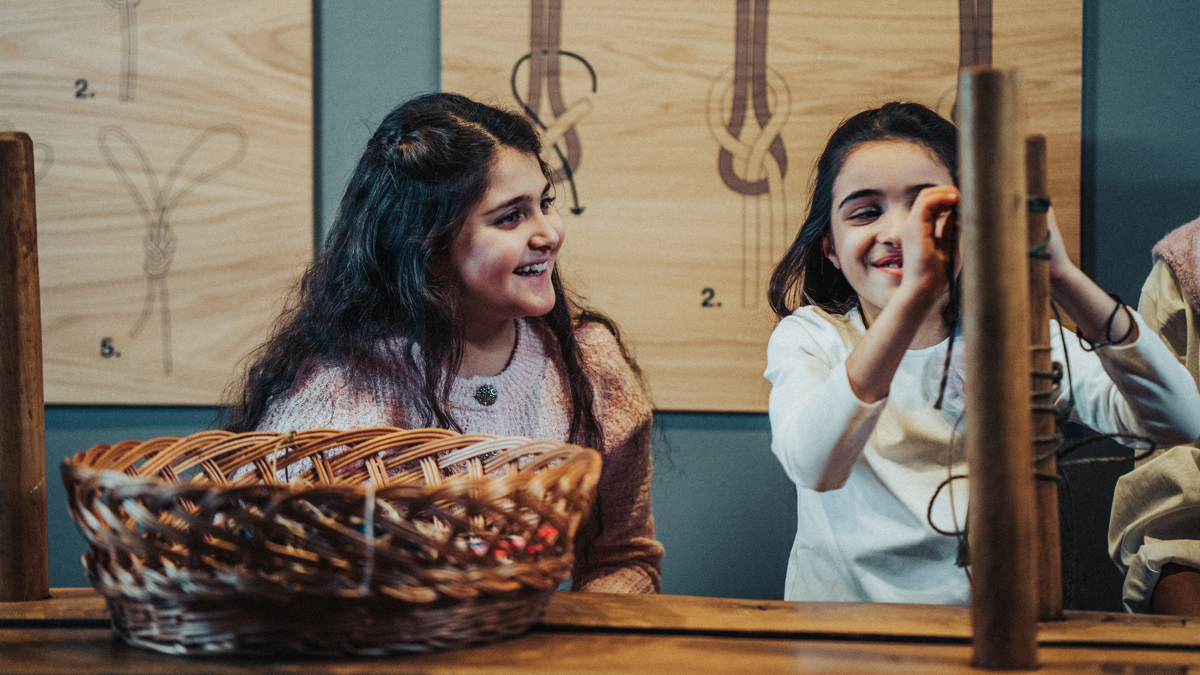 Två barn sitter vid ett bord på Marinmuseum och lär sig knyta knopar, skrattande och fokuserade framför träskyltar som visar olika knopar.