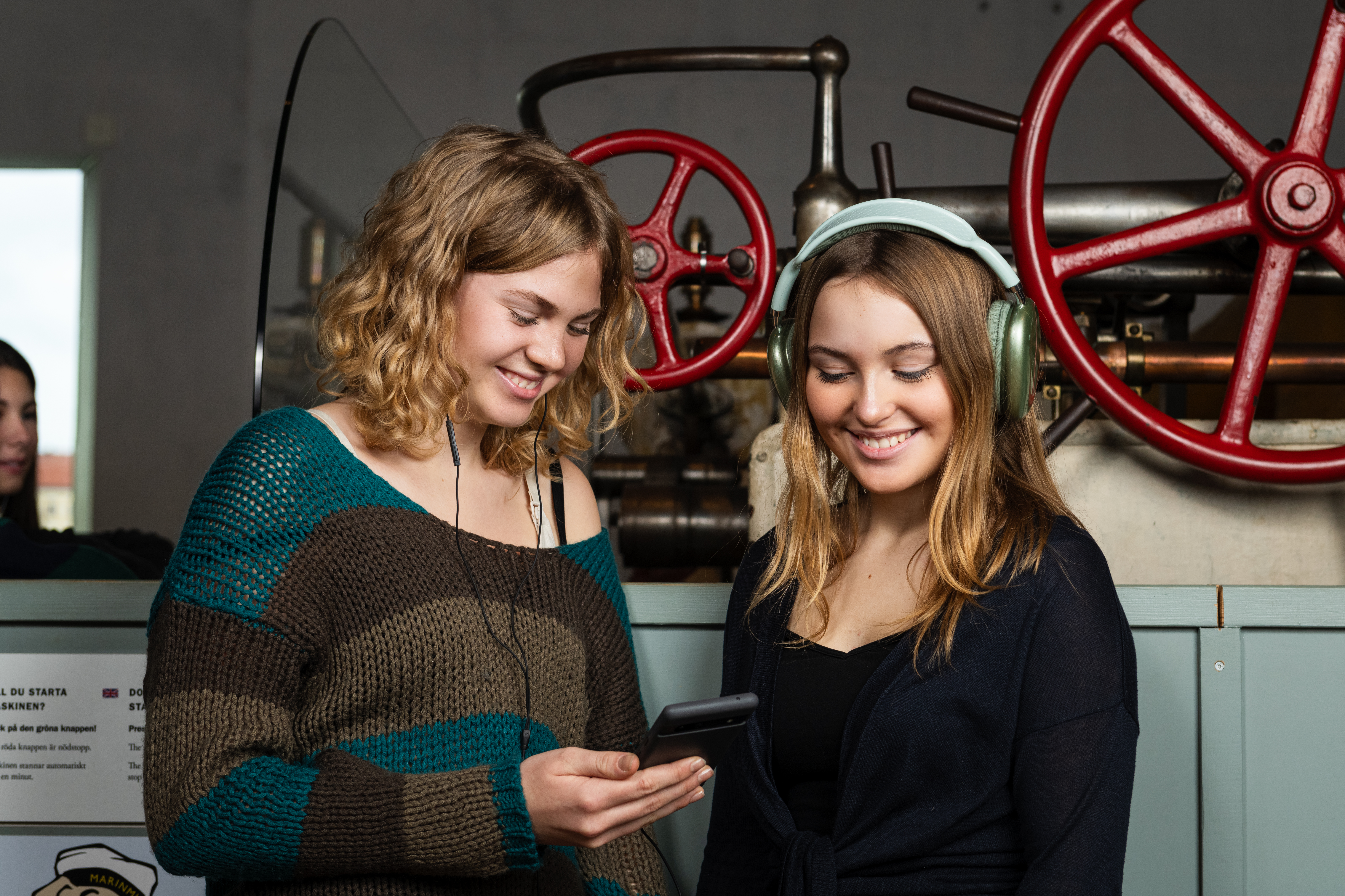 Two happy young women with headphones are looking at a mobile phone in a museum.