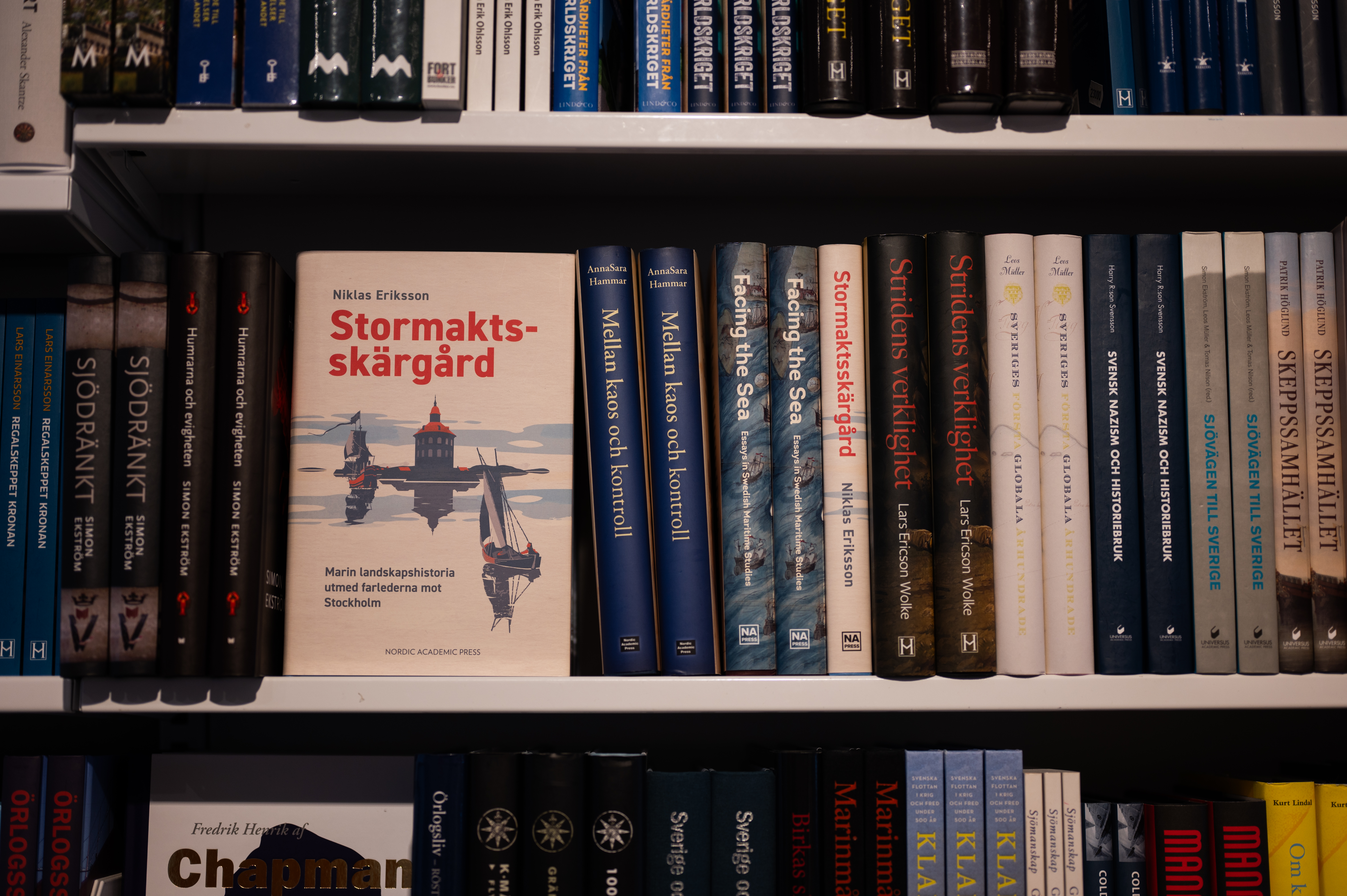 En bokhylla fylld med historiska böcker där titeln Stormaktsskärgård syns tydligt i mitten.