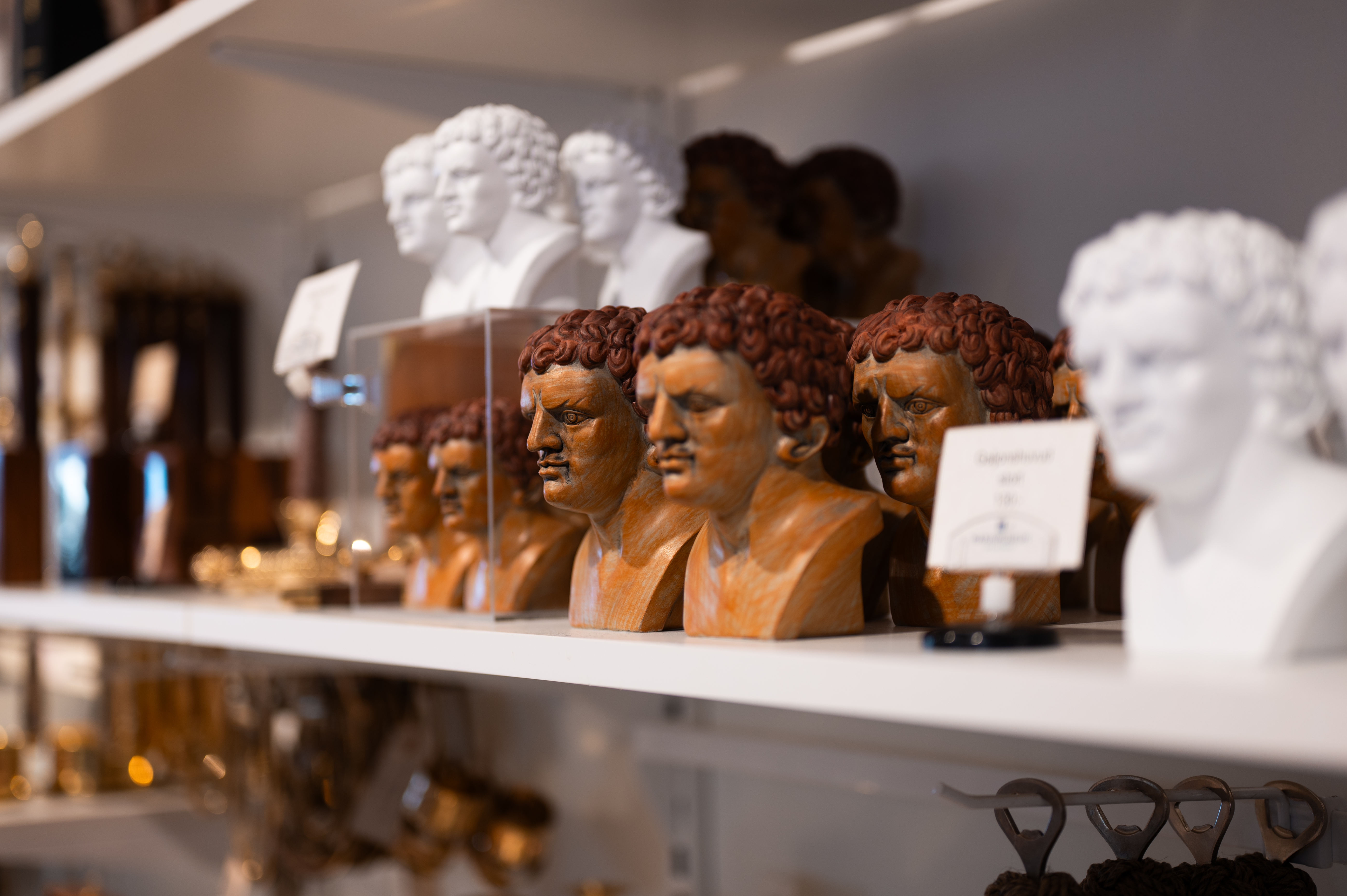 Hylla med flera små byster i vitt och träfärg i en butiksmiljö