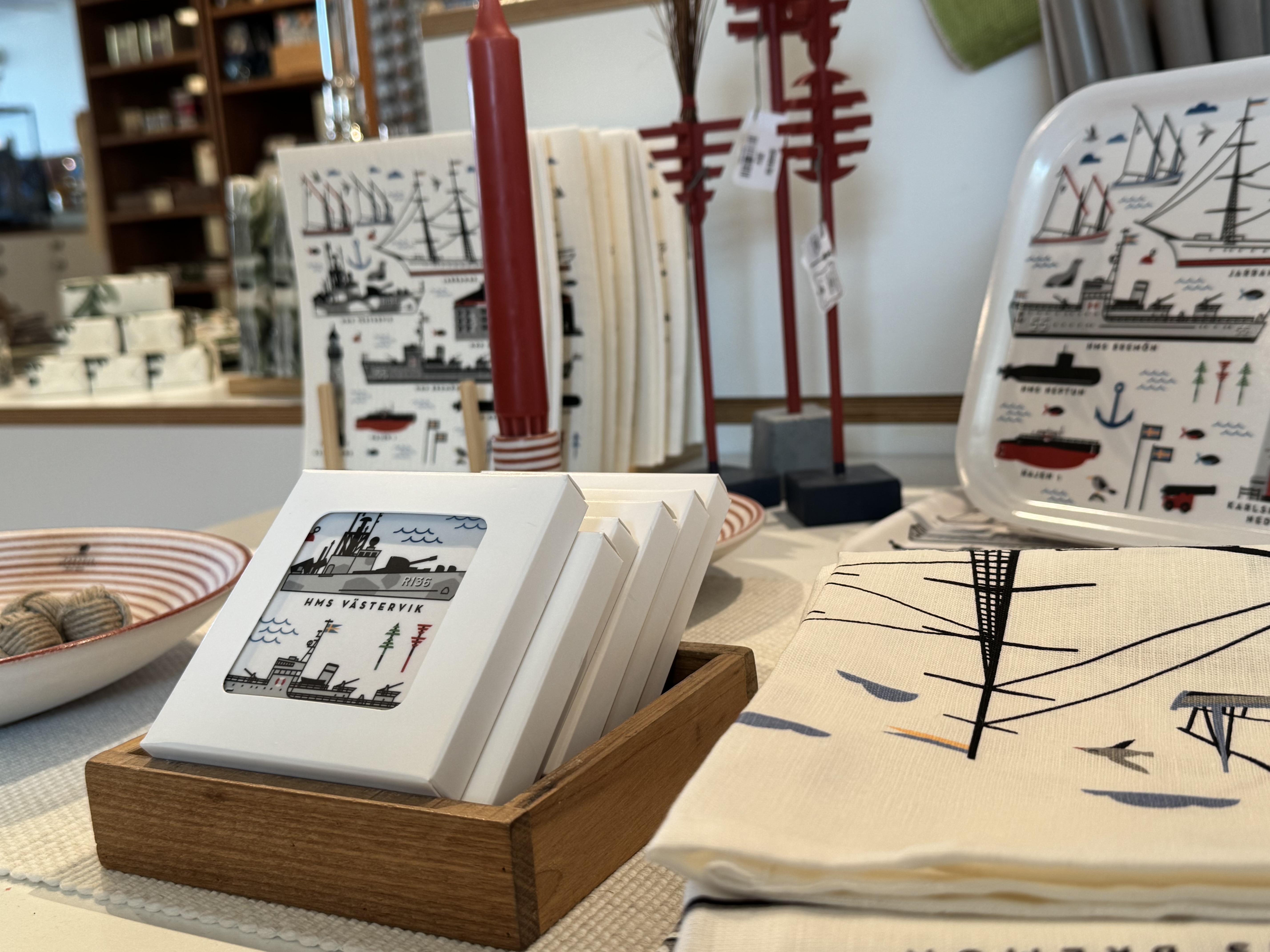 Närbild av souvenirer i museibutiken på Marinmuseum, med brickor, underlägg och textilier med marina motiv i rött, blått och svart.