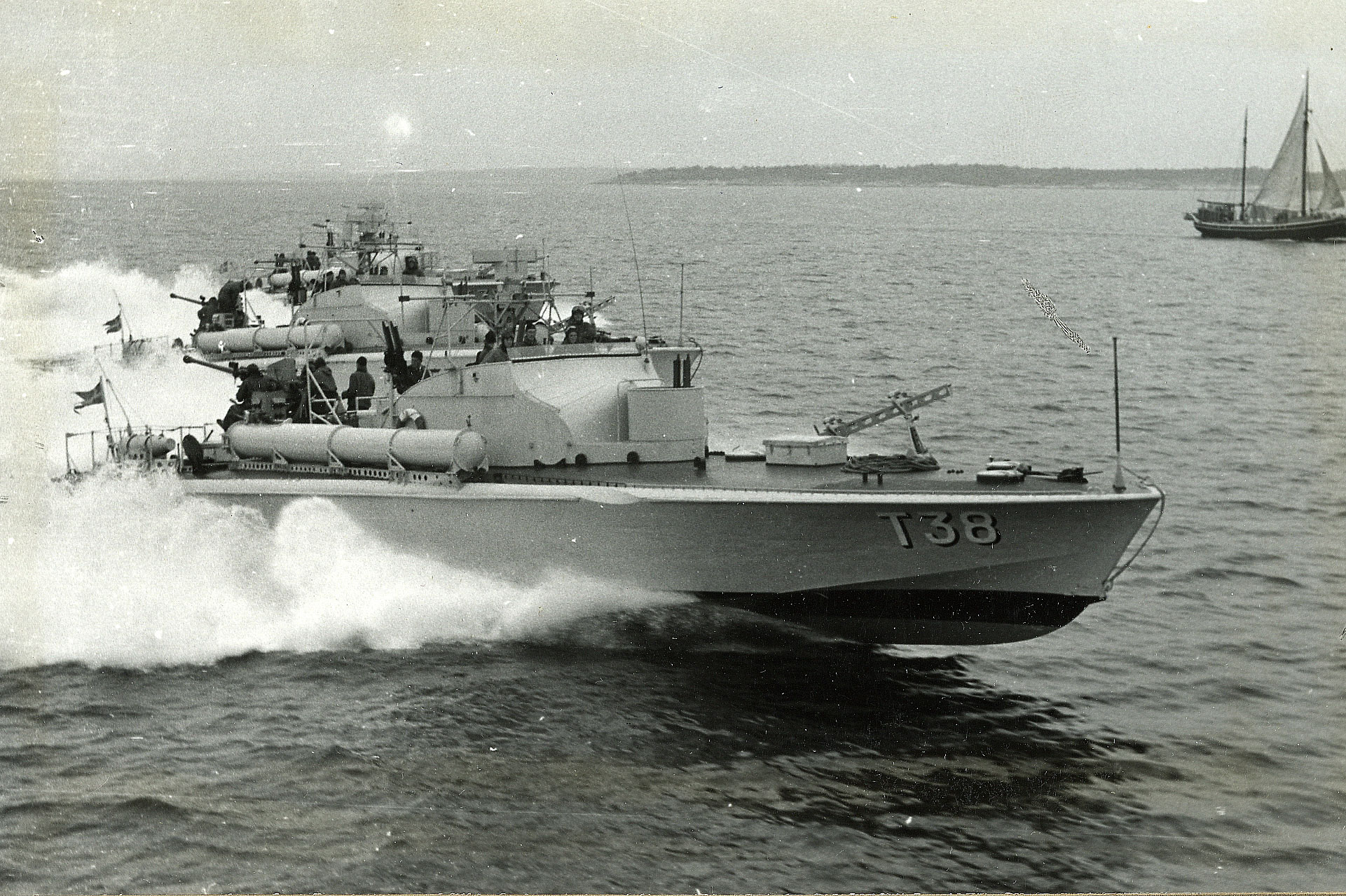 Två torpedbåtar ur svenska marinen navigerar i hög fart genom en skärgård, med skummande svall bakom sig.