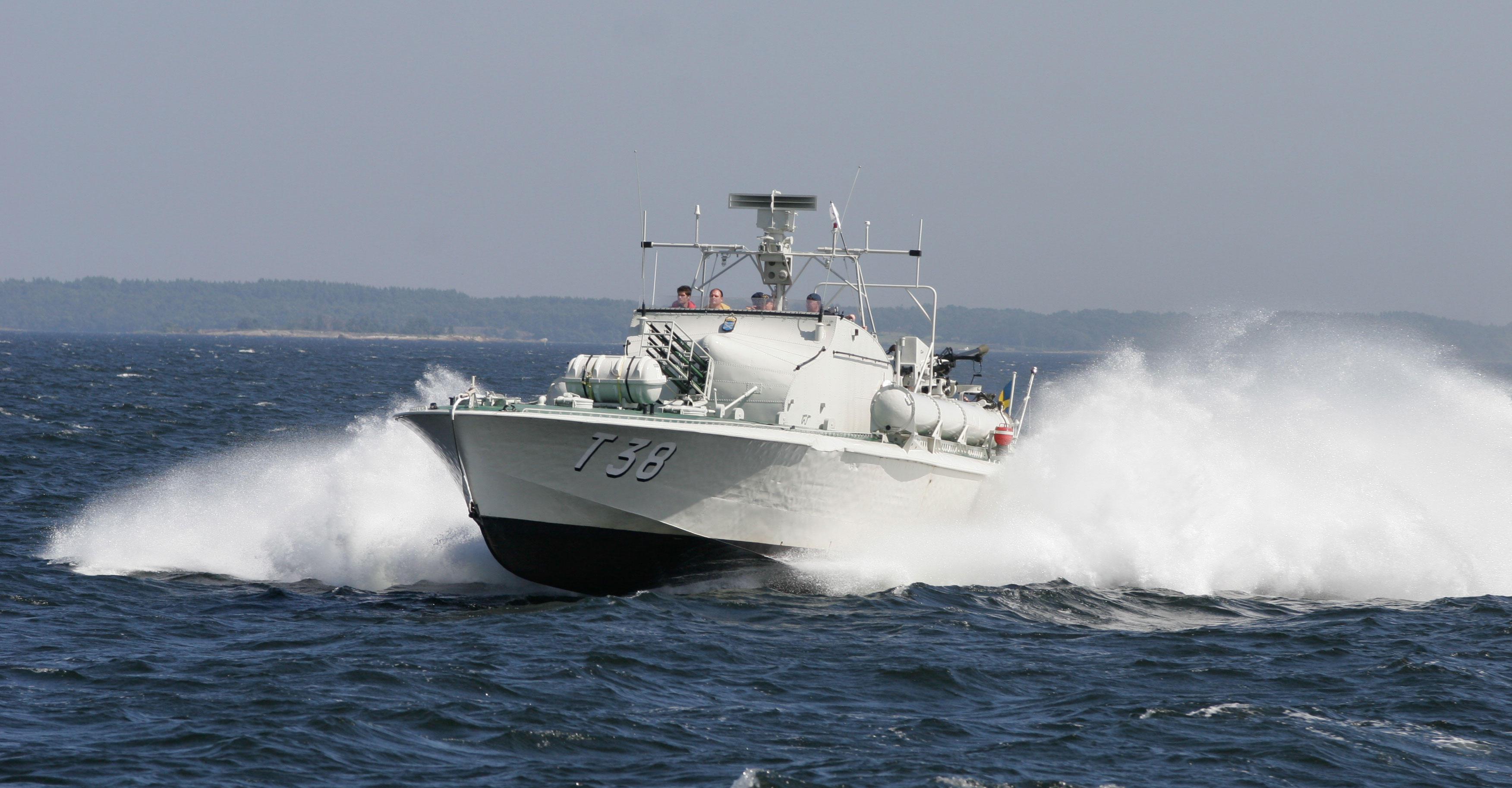 En svensk torpedbåt med beteckningen T38 färdas i hög fart över öppet hav, vatten stänker högt upp vid båtens för.