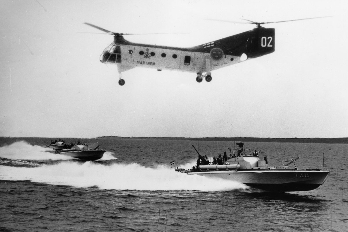 Tre torpedbåtar eskorteras av en marinhelikopter under en övning till havs, med T38 i förgrunden.