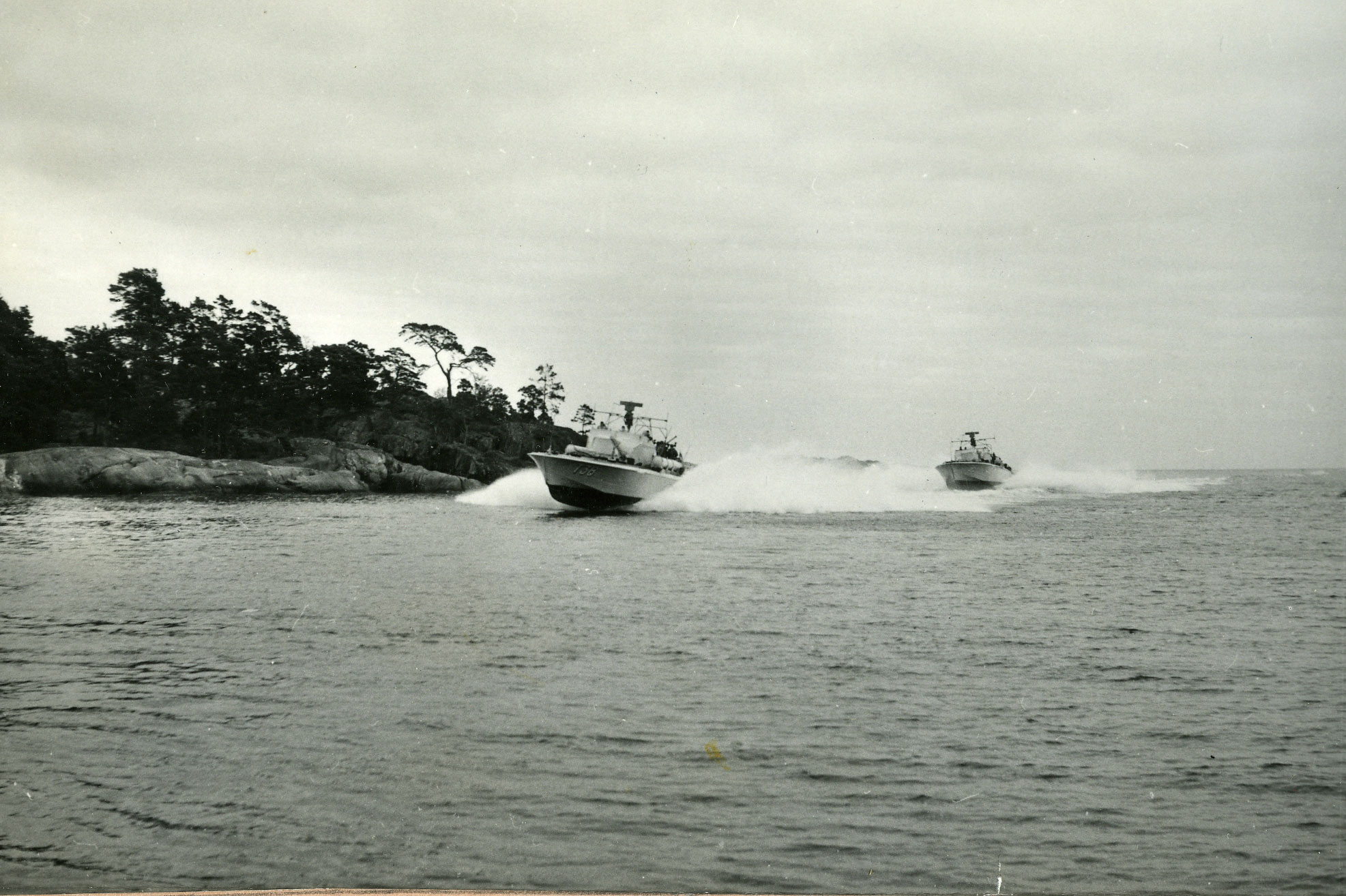 Flera torpedbåtar ur svenska flottan, ledda av T38, kör i hög hastighet på öppet vatten med besättningarna synliga på däck.