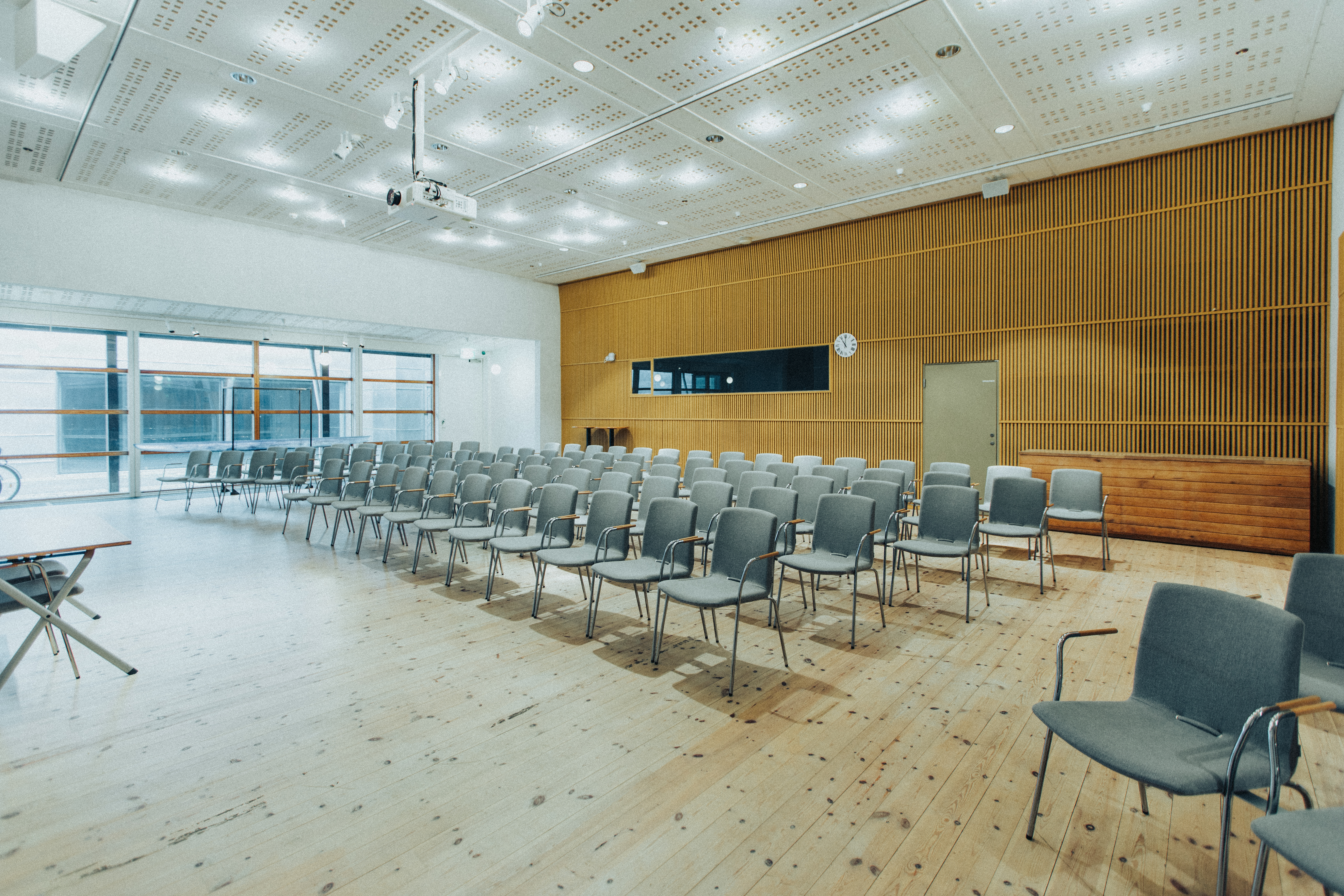 Ett ljust föreläsningsrum med tomma stolsrader, podium och stor skärm.