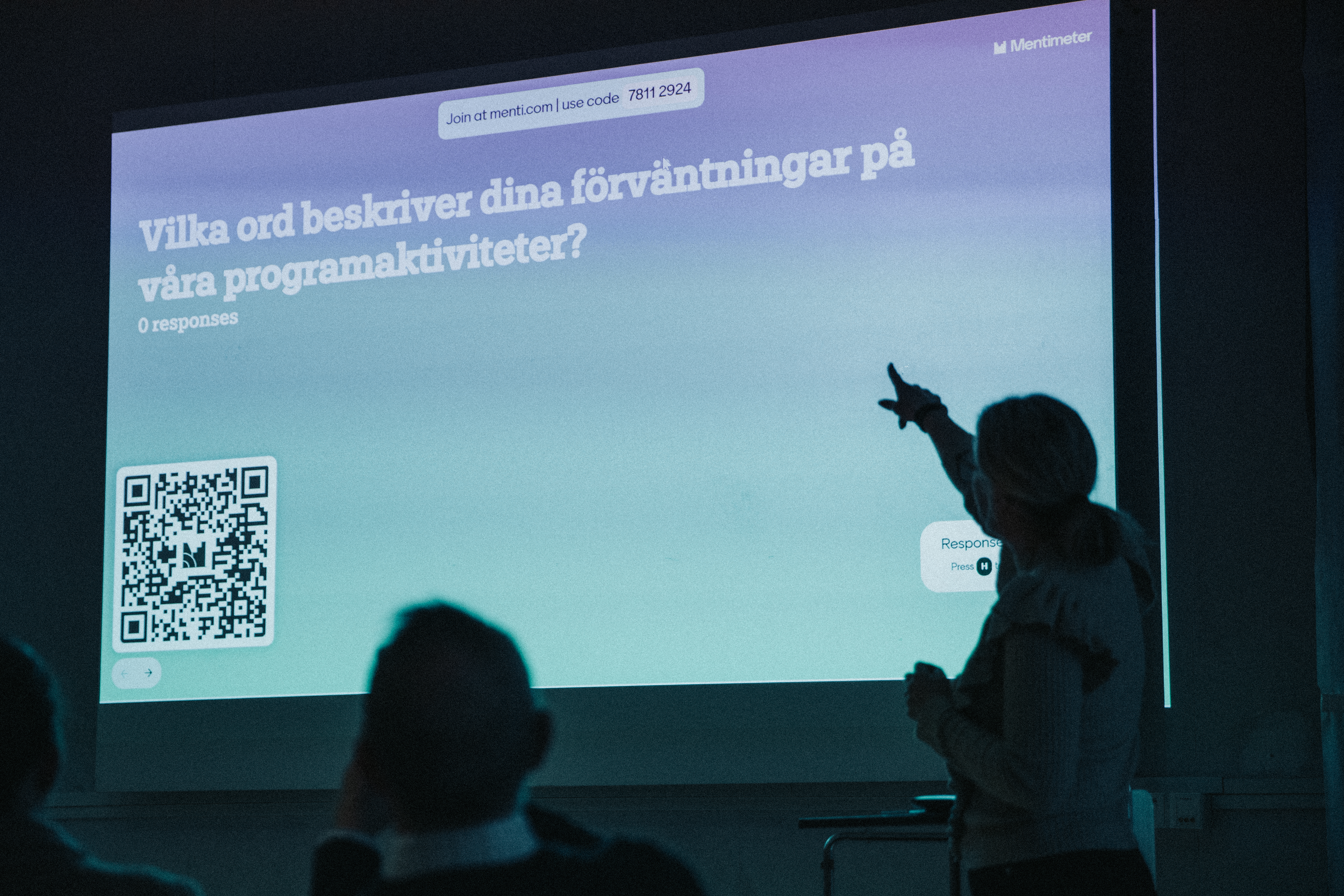 Person som presenterar framför en projicerad bild i ett mörkt rum.