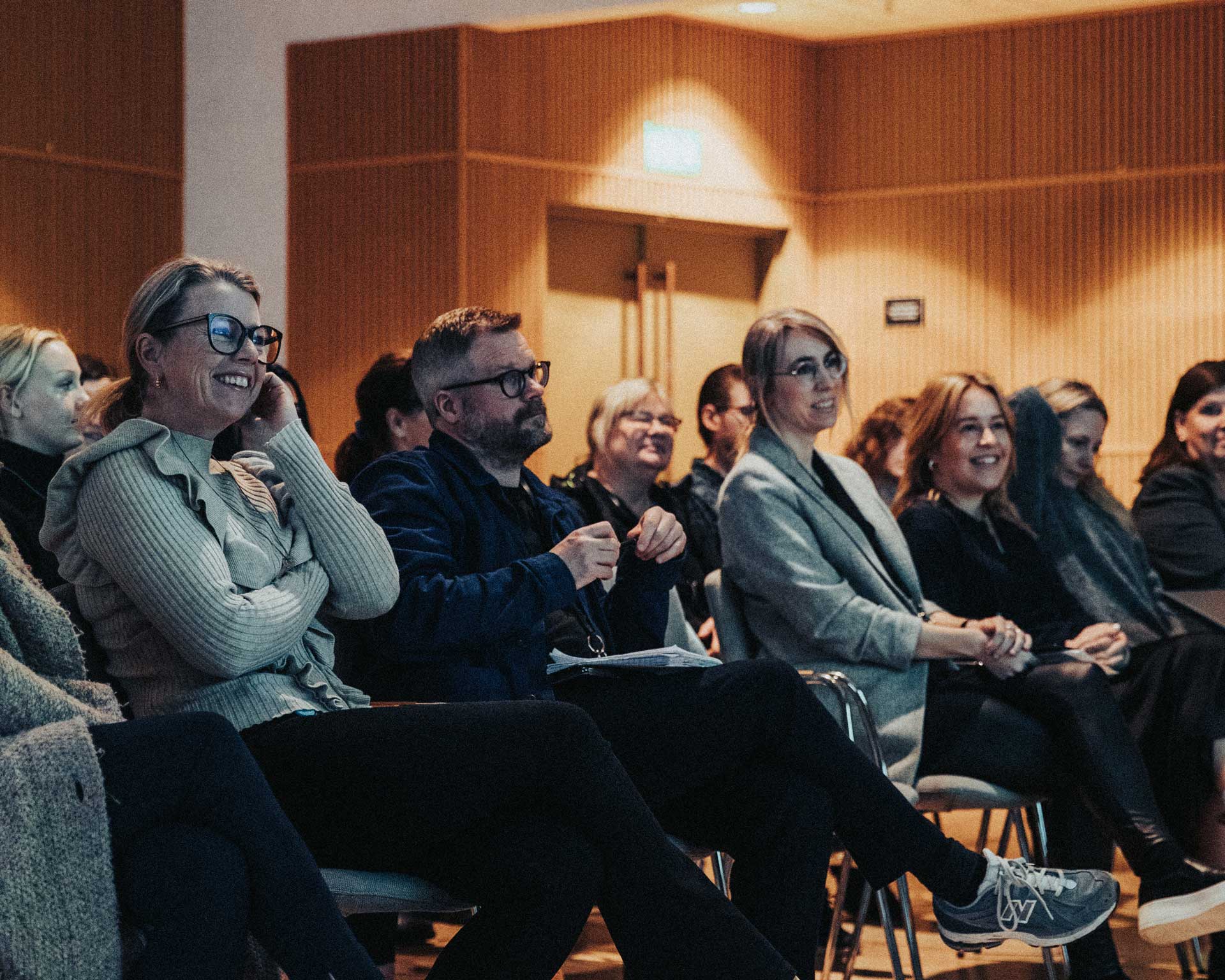 Flera personer sitter på stolar och tittar åt samma håll i ett konferensrum.