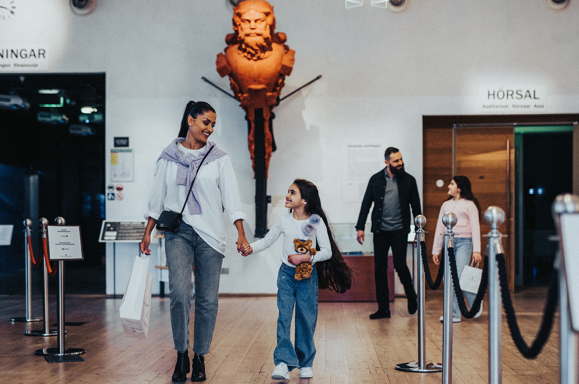 A family walks through the entrance hall at the Naval Museum with a figurehead in the background.