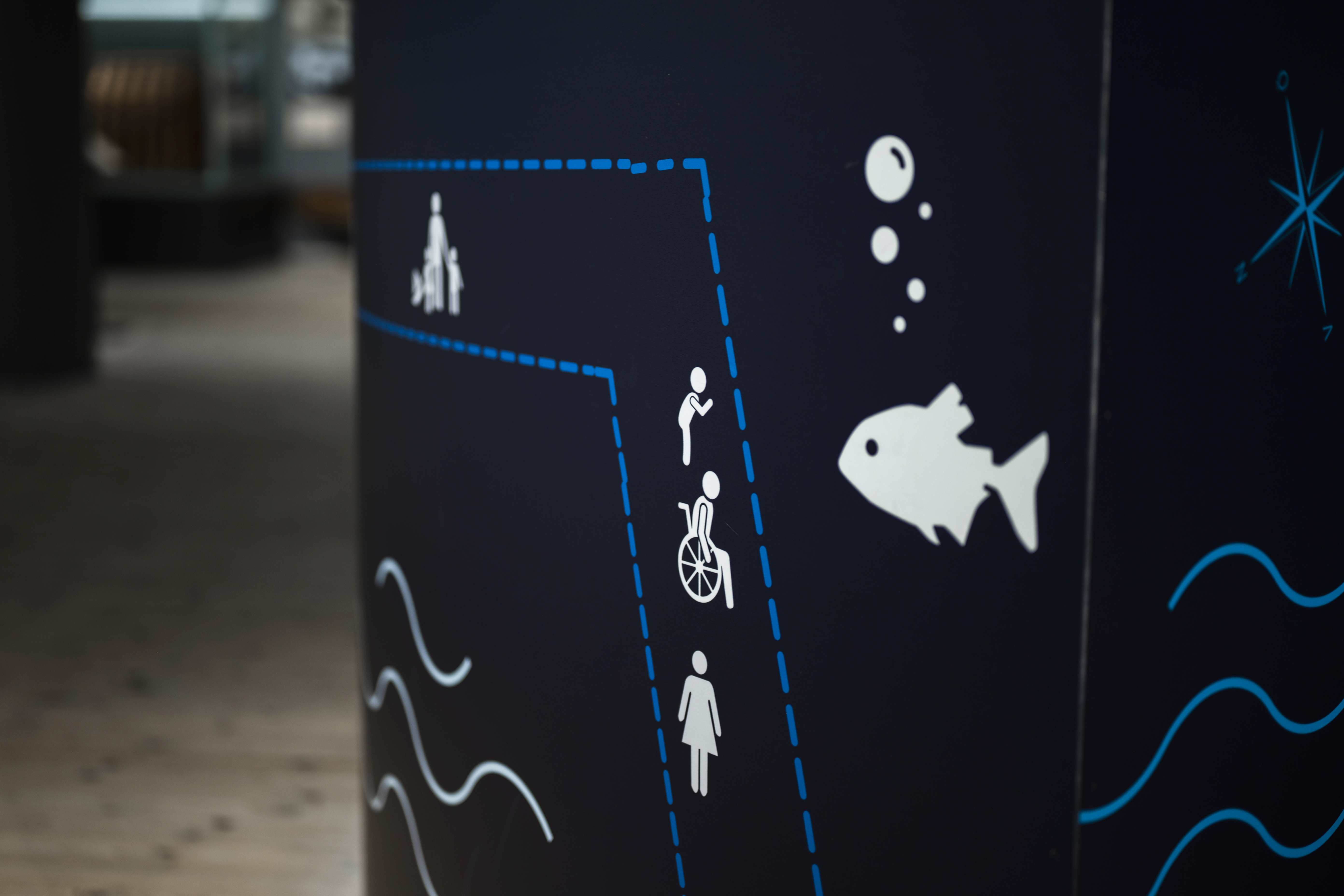 A dark blue sign at the Naval Museum showing accessibility and wayfinding symbols.