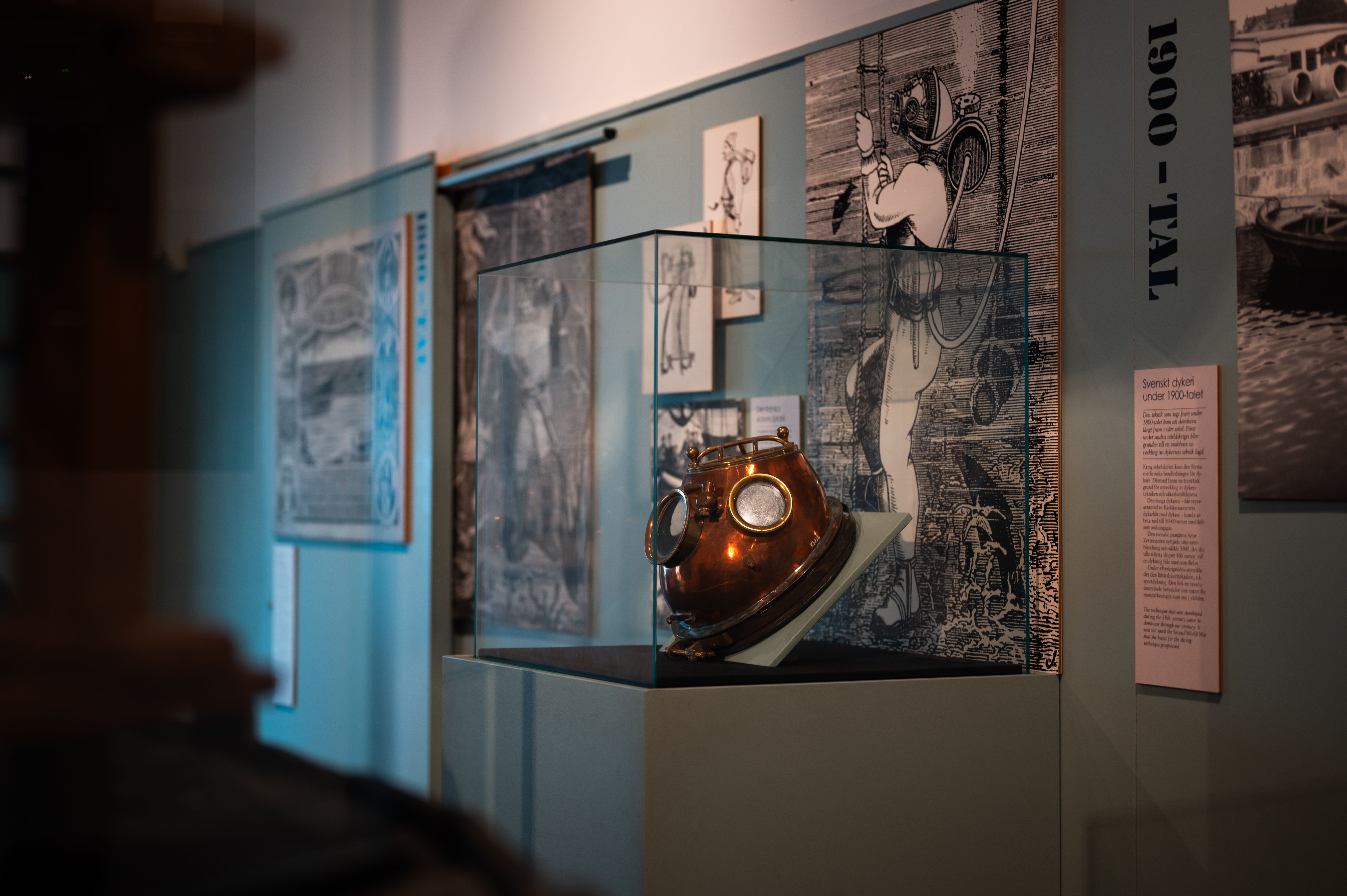 A historical version of a diving helmet is displayed in a glass case.