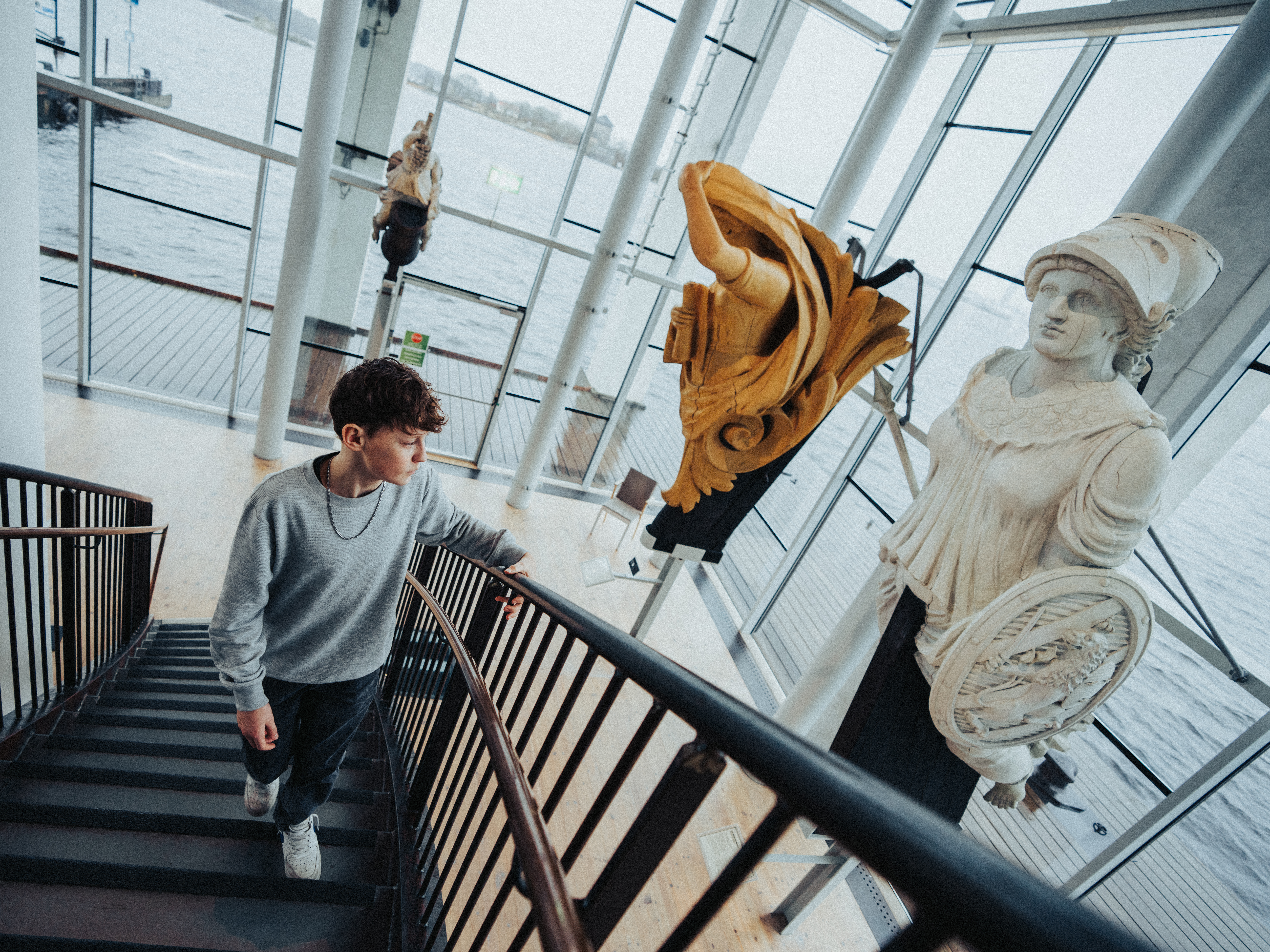 En person går uppför trappan i Galjonshallen på Marinmuseum, omgiven av stora galjonsfigurer i trä.