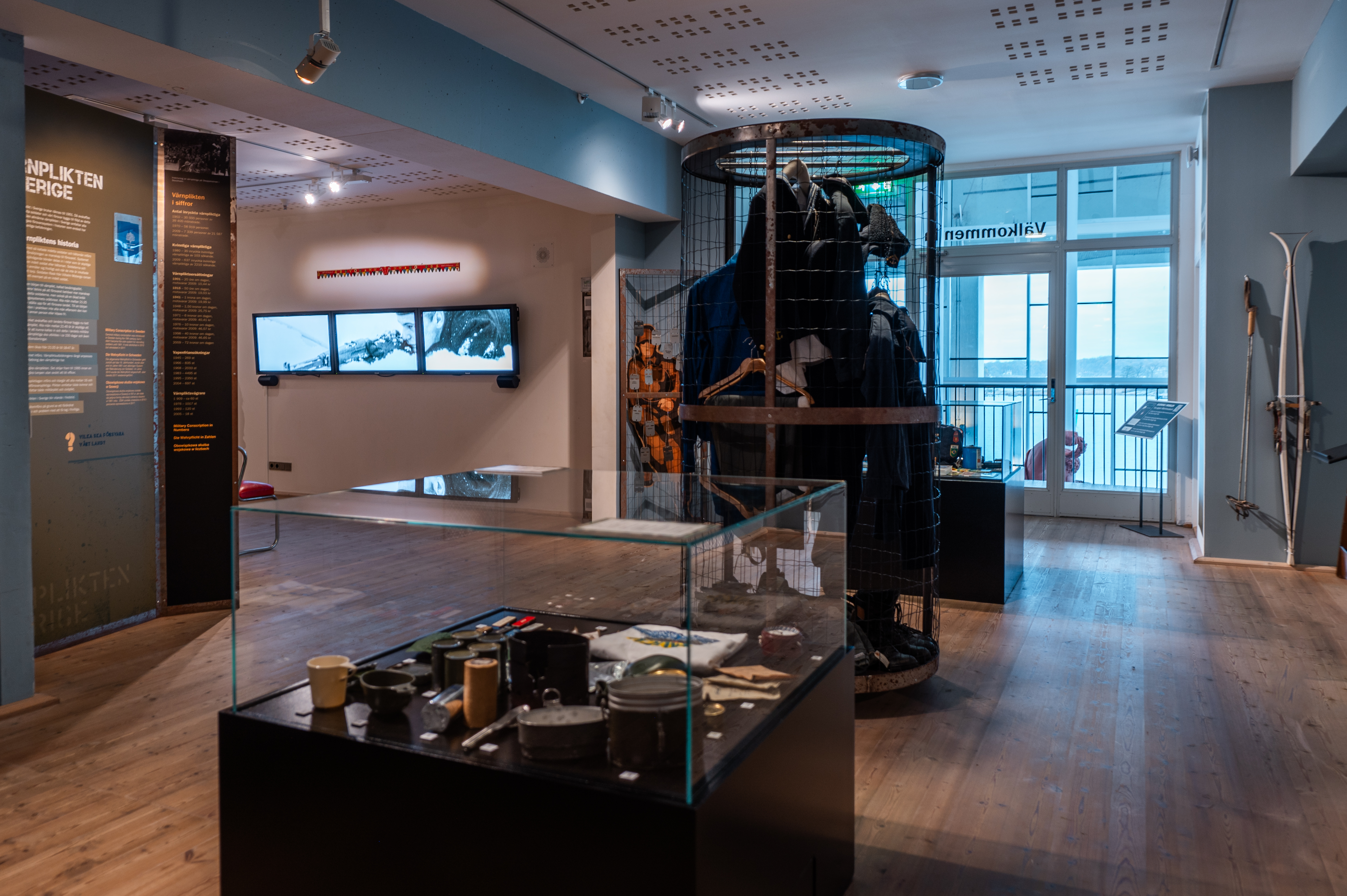 Bilden visar museiutställningen med uniformer, föremål och information om värnplikt. Föremål visar i glasmontrar och på väggar. 