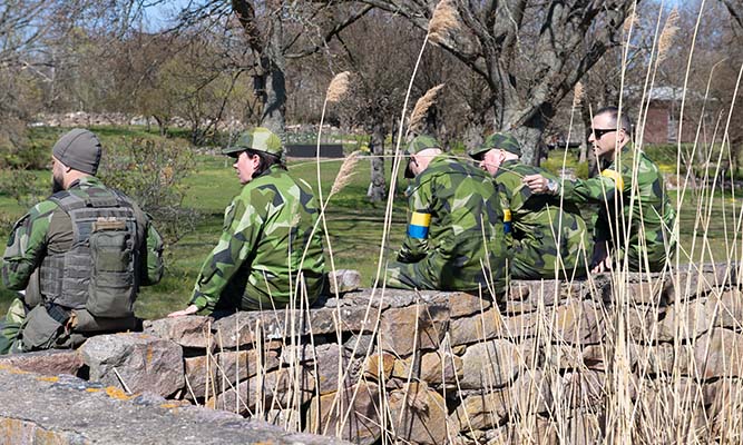 A group of people in camouflage clothing are sitting on a stone wall.