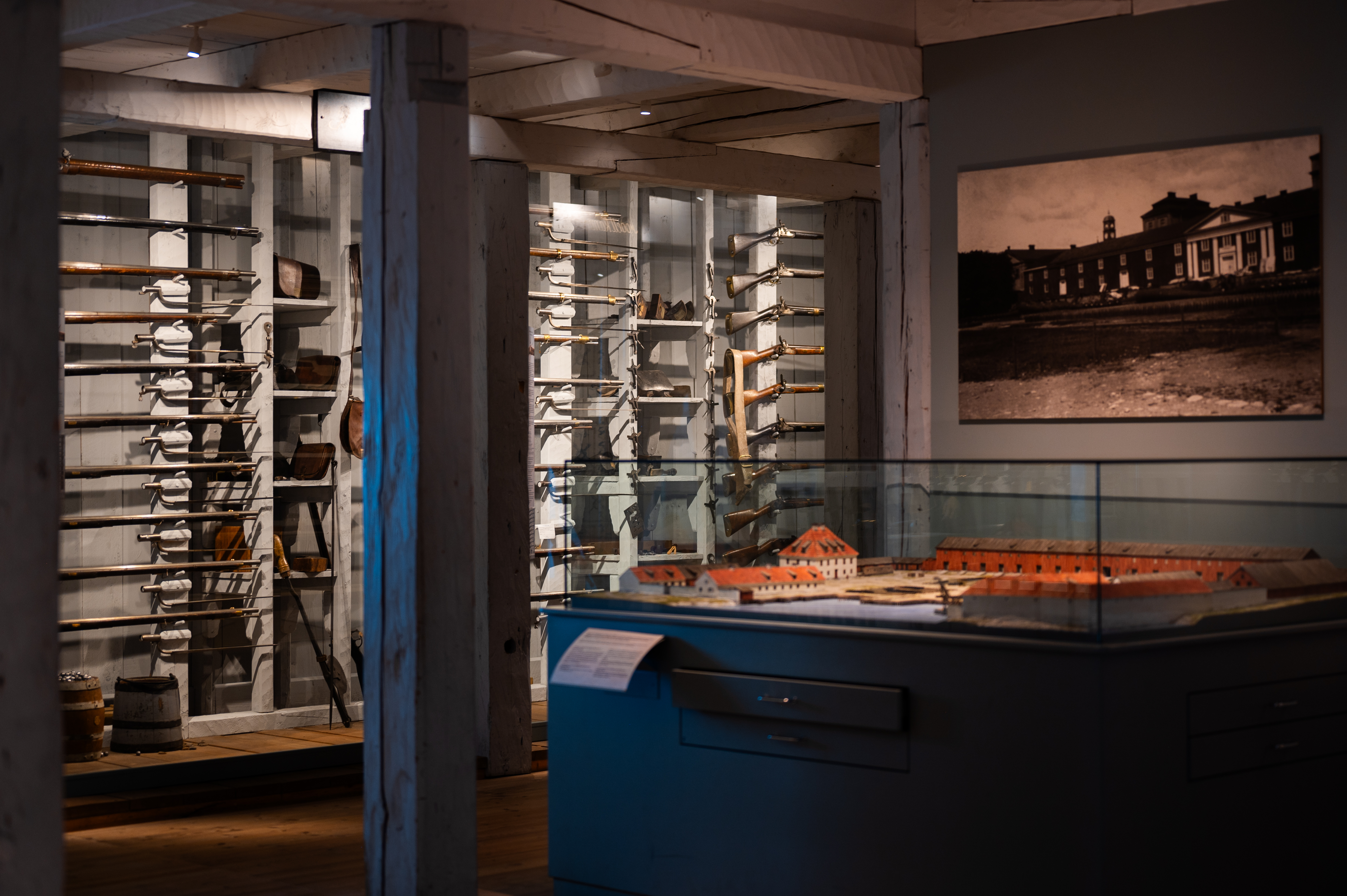 About ten weapons are visible behind a glass case. In front of them are miniatures of various buildings in a glass case.