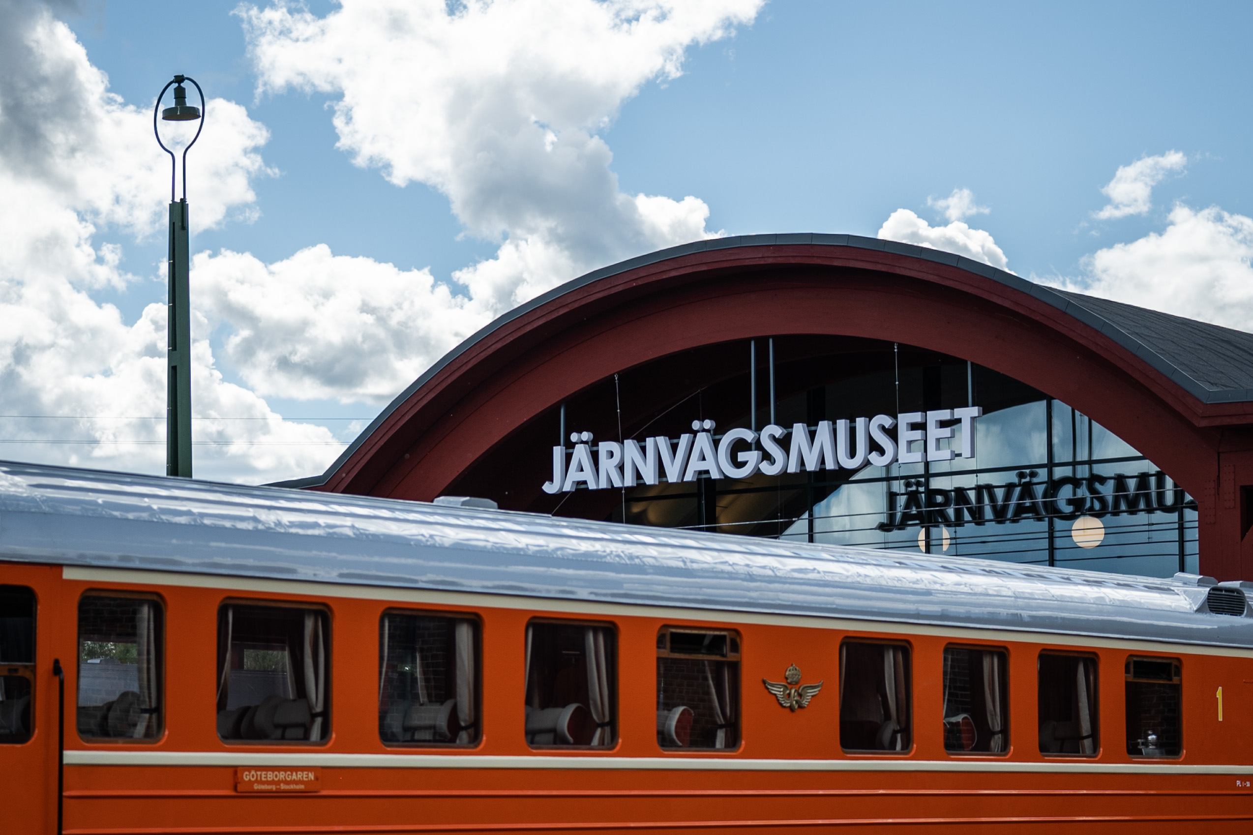 Entrén till Järnvägsmuseet med ett orange tåg i förgrunden.