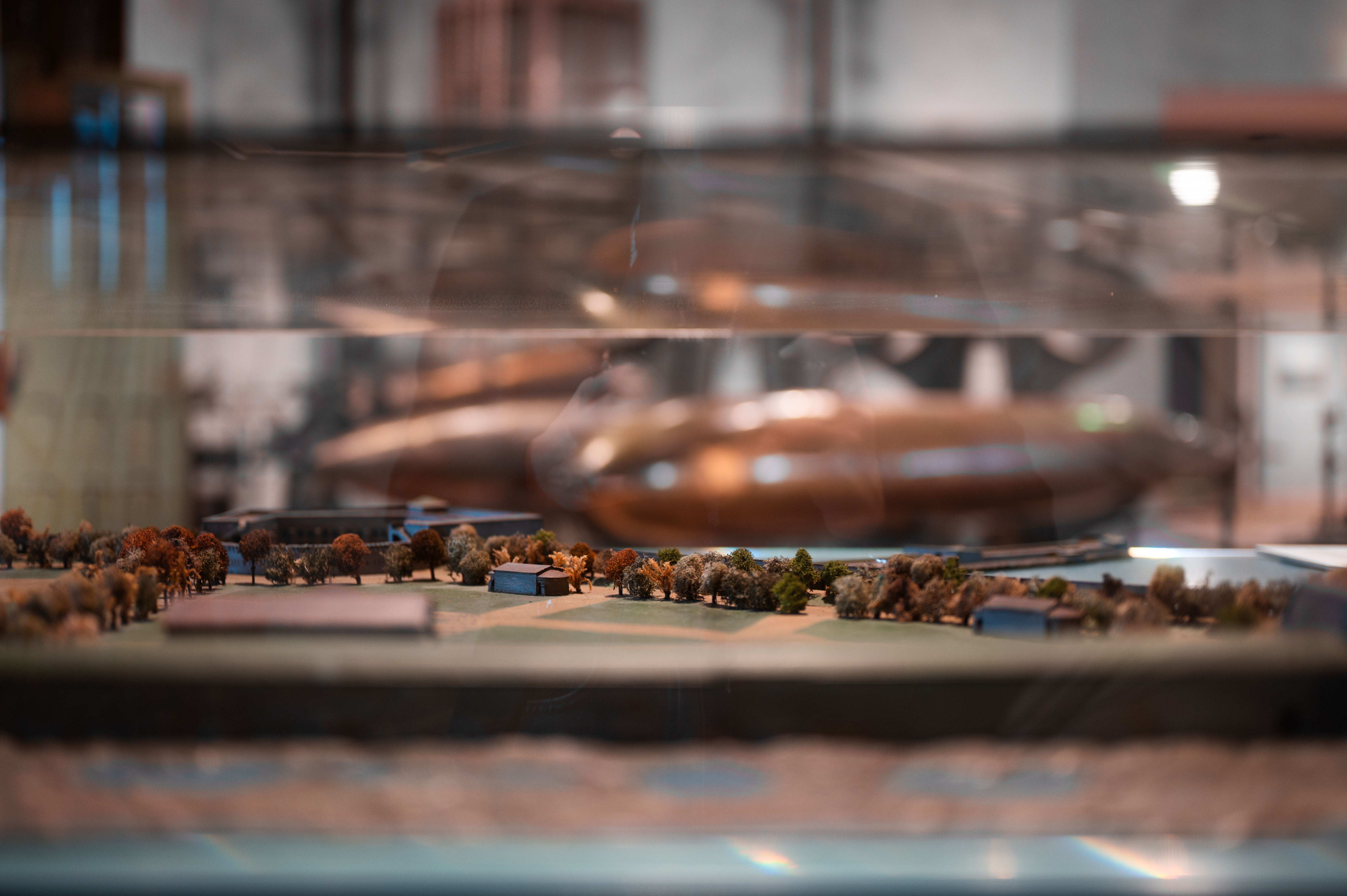 Detaljbild av en miniatyrmodell med byggnader och träd i en monter på Marinmuseum, med reflektioner av föremål i bakgrunden.