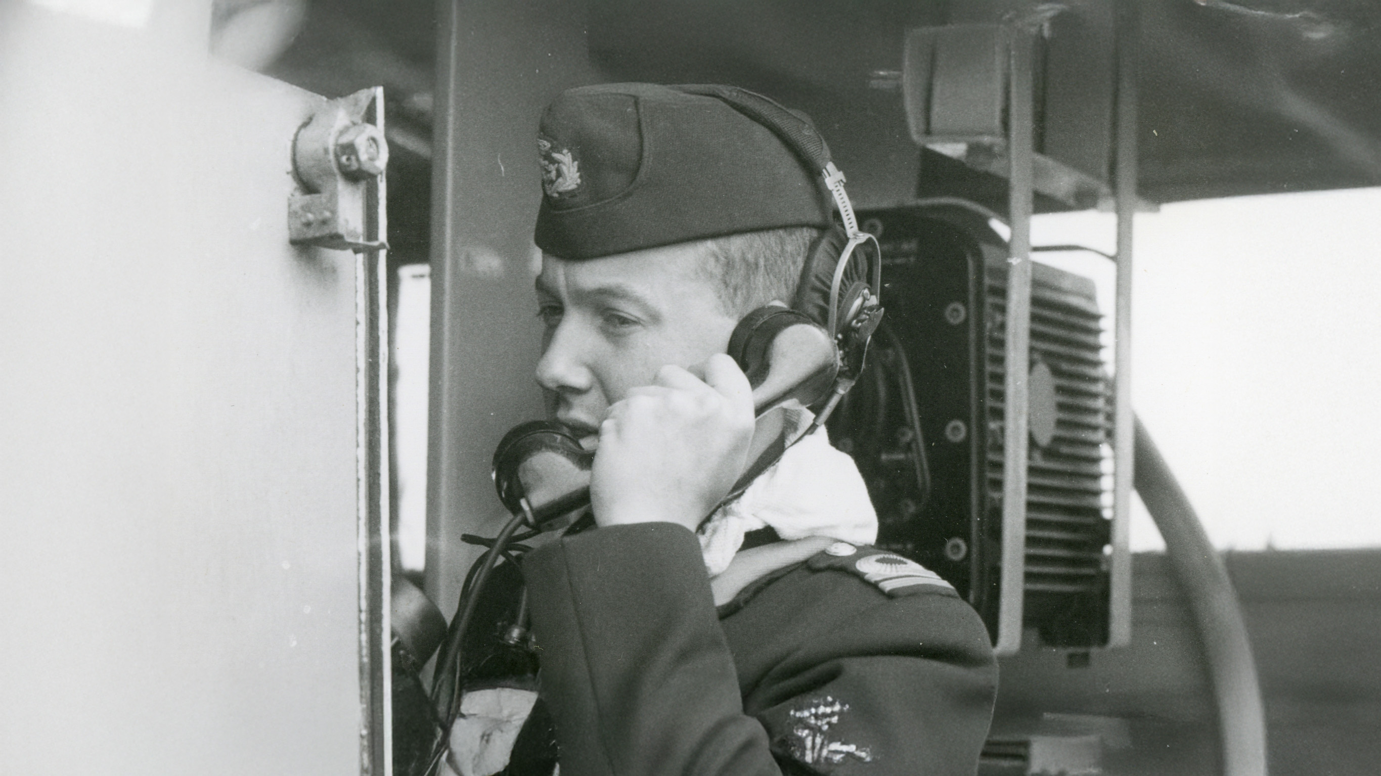 En svartvit bild som visar en officer i uniform som kommunicerar via telefon på ett fartyg.