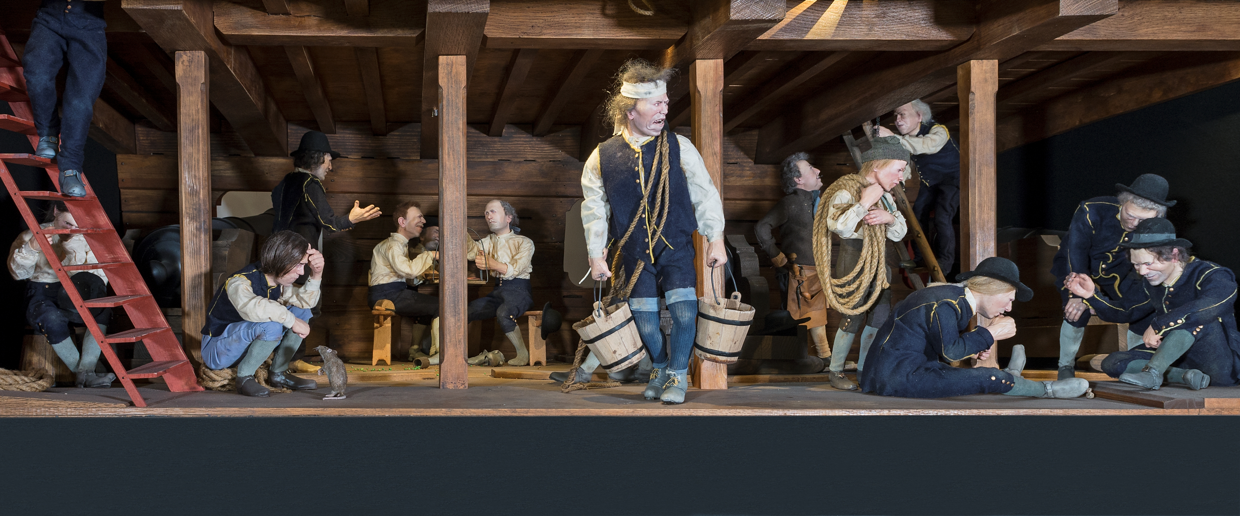 En detaljerad scen visar sjömän i historiska kläder som arbetar, vilar och umgås ombord på ett träfartyg.