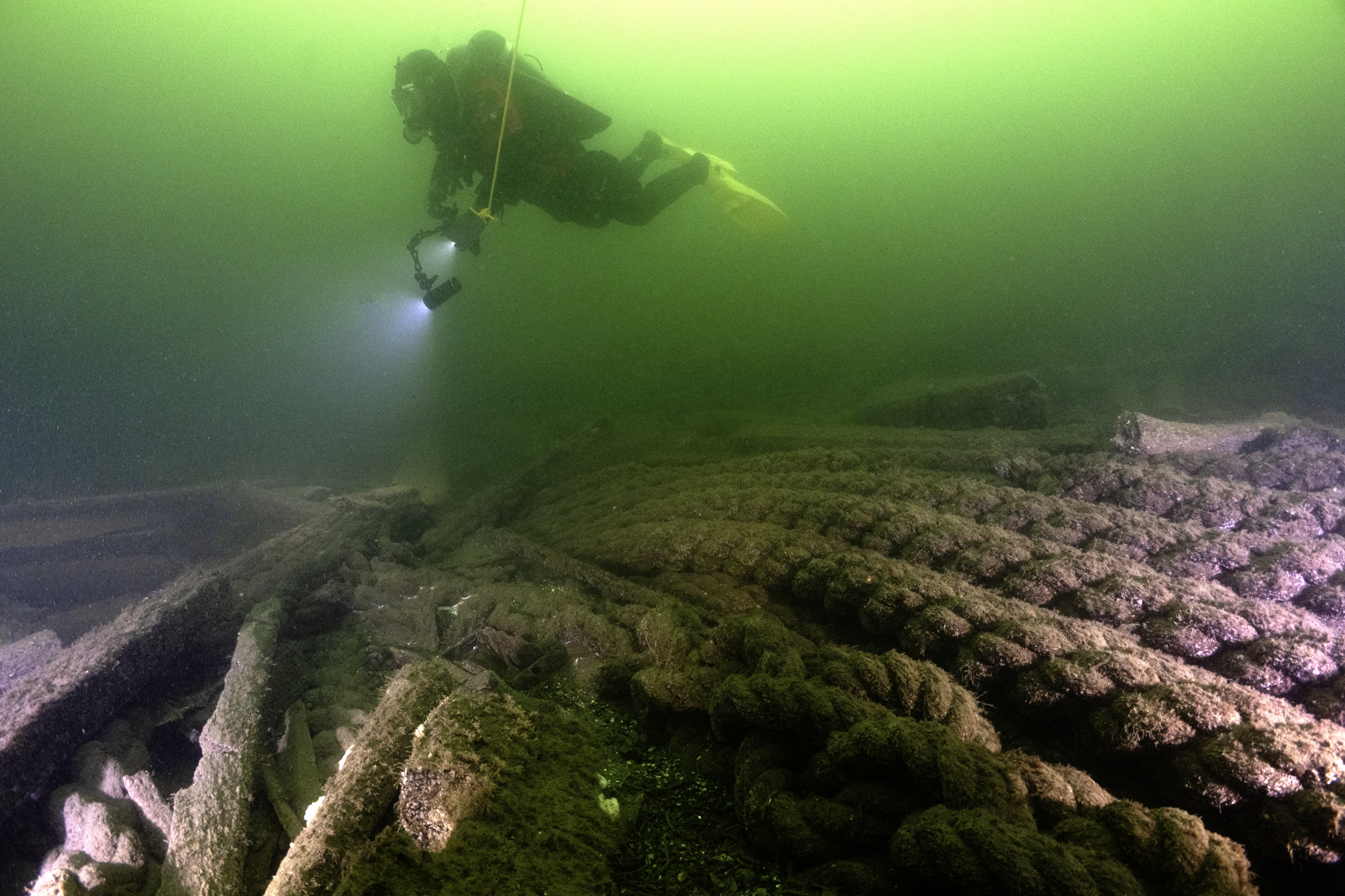 En dykare dokumenterar ett historiskt skeppsvrak på Östersjöns botten med hjälp av kamera och belysning.